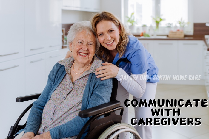 A smiling caregiver leaning over to engage with a happy elderly woman seated in a wheelchair in a bright kitchen. This image highlights the importance of open communication between caregivers and clients, showcasing the compassionate home nursing services of Jai Sri Ohm Sakthi Home Care in Coimbatore